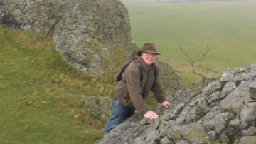 Mann klettert über Felsen in grüner Hügellandschaft